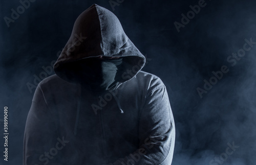 Obraz na plátně A hooded man with a face mask waits in the dark