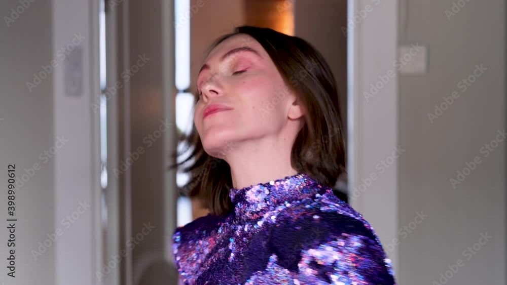 Attractive young woman with short hairstyle in trendy purple dress poses for camera showing gesture Horns in room closeup Attractive young woman with short hairstyle in trendy purple dress poses for camera showing gesture Horns in room closeup