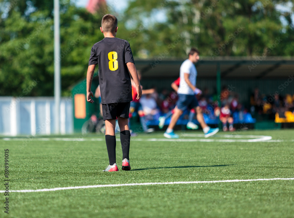 Boys in black sportswear plays football on field, dribbles ball. Young soccer players with ball on green grass. Training, football, active lifestyle for kids