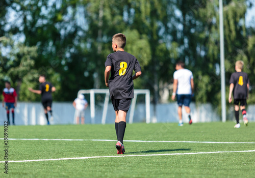 Boys in black sportswear plays football on field, dribbles ball. Young soccer players with ball on green grass. Training, football, active lifestyle for kids