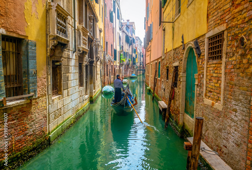 Venetian gondolier punting gondola through green canal waters of Venice Italy © Pawel Pajor