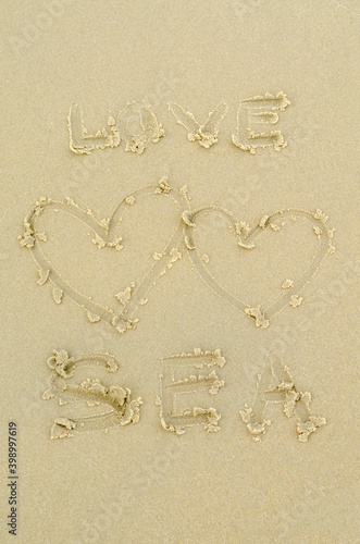 handwritten love sea text with two hearts on sand