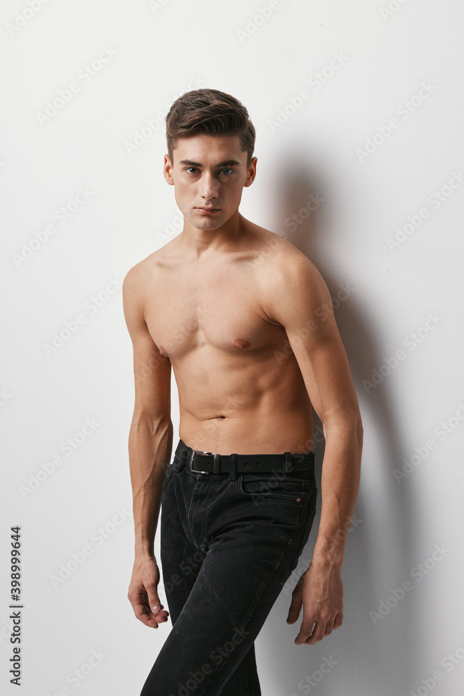 A man with a naked torso and in trousers on a light background A man with a naked torso and in trousers on a light background