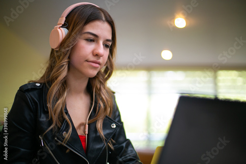 Young woman with headphones sitting in front of her computer, she is doing her homework
