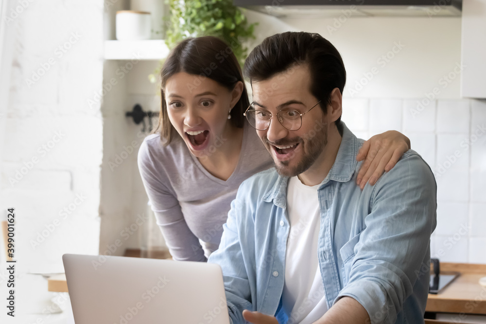 Close up amazed young couple looking at laptop screen, sitting at table in kitchen at home, overjoyed family received unbelievable great news, mortgage or loan approval, online lottery win Close up amazed young couple looking at laptop screen, sitting at table in kitchen at home, overjoyed family received unbelievable great news, mortgage or loan approval, online lottery win