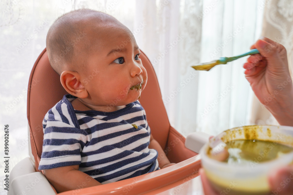 An asian kid boy in high chair or feeding table eating healthy food. Concept of child food, family care and child eats food. An asian kid boy in high chair or feeding table eating healthy food. Concept of child food, family care and child eats food.