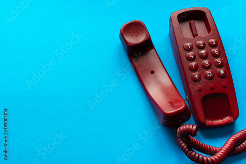 Red Old fashion landline home phone with handset off hook, on wire on light blue background with blank space for text.  Answer call. Pick up phone. Hang up phone. Copy space