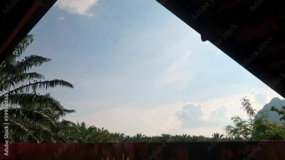 Low angle view under house roof top of white cloud moving on sunny blue sky background over concrete cement fence with tropical summer rain-forest palm tree plantation n mountain, 4k b-roll TimeLapse Low angle view under house roof top of white cloud moving on sunny blue sky background over concrete cement fence with tropical summer rain-forest palm tree plantation n mountain, 4k b-roll TimeLapse