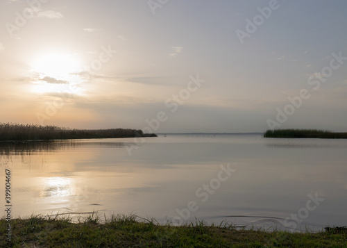 view of the lake before sunset  sunbeams through the clouds  calm water surface  lake meadow foreground
