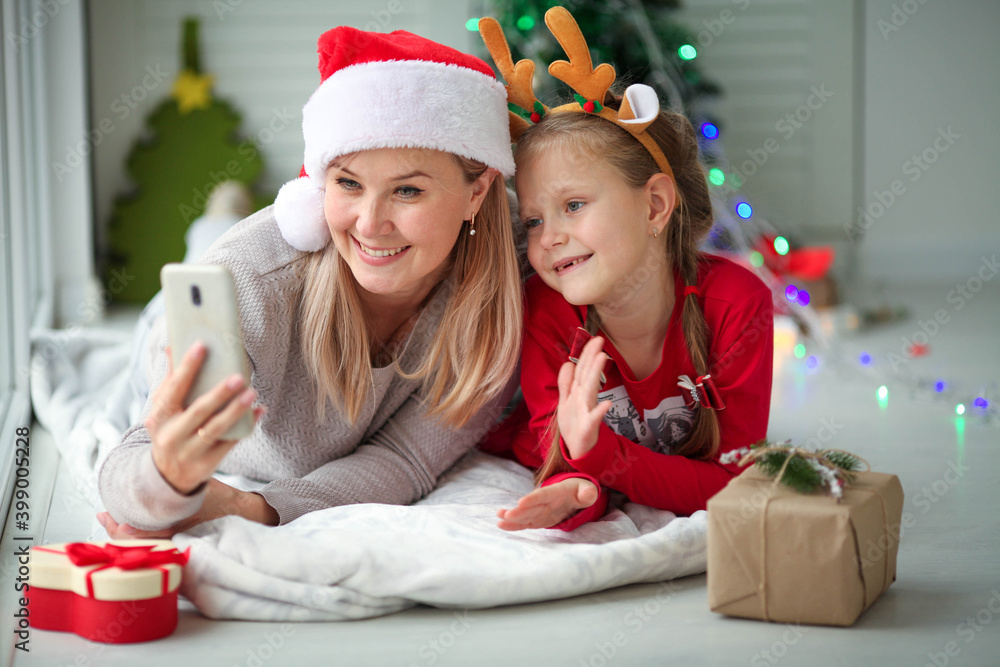 Mom and daughter wish Happy New Year by mobile phone for video calls to father, family, friends. Christmas online holiday remote celebration of Christmas in isolation from coronavirus. Mom and daughter wish Happy New Year by mobile phone for video calls to father, family, friends. Christmas online holiday remote celebration of Christmas in isolation from coronavirus.