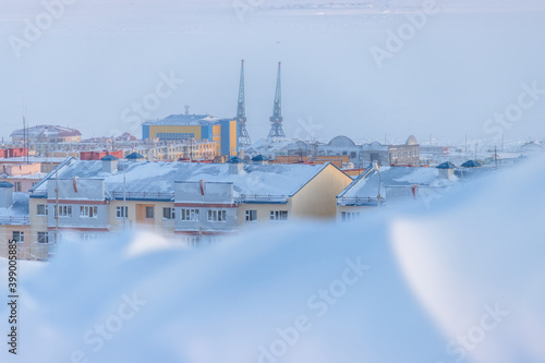 Winter view of a snow-covered northern city in the Arctic. Roofs of buildings. Cold frosty winter weather. A lot of snow. Harbor cranes in the distance. Anadyr, Chukotka, Siberia, Far North of Russia.