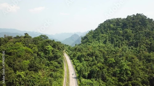 Drone shot of a driver on a motorbike on an empty road in the middle of the jungle in Quang Binh Province near Dong Hoi, Vietnam with mountains in the background on a sunny day.