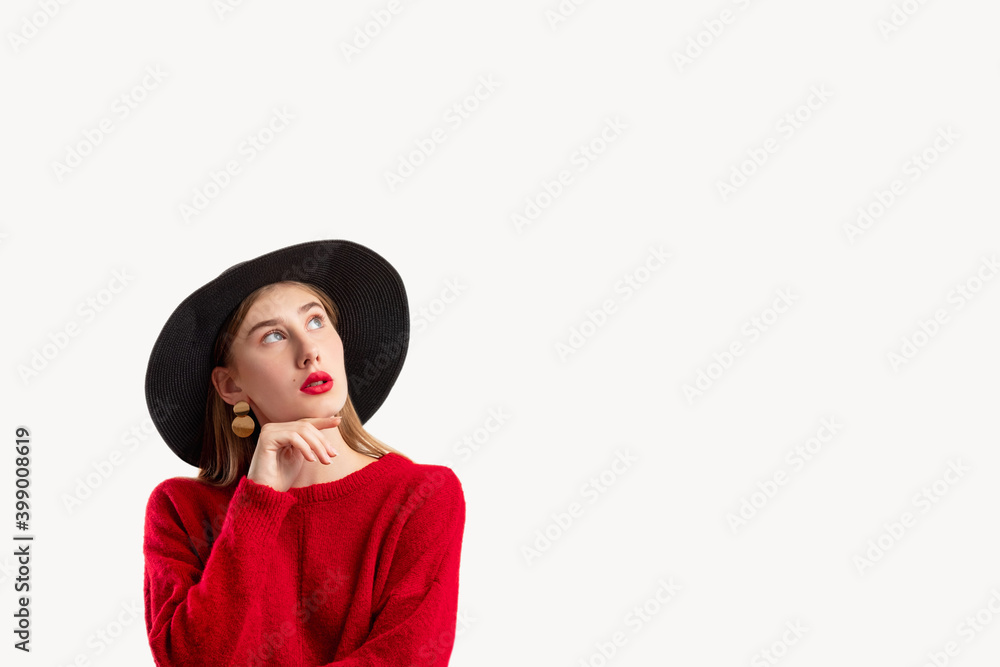 Doubtful female model. Create idea. Trend look. Personal offer. Information banner. Thoughtful woman in red sweater black hat holding chin looking up isolated on white copy space.