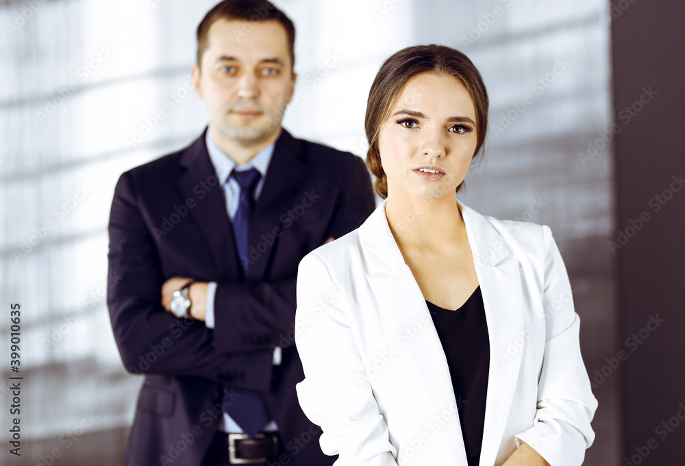 Young beautiful businesswoman is standing in an office with a male colleague at the background. Concept of success in a business Young beautiful businesswoman is standing in an office with a male colleague at the background. Concept of success in a business
