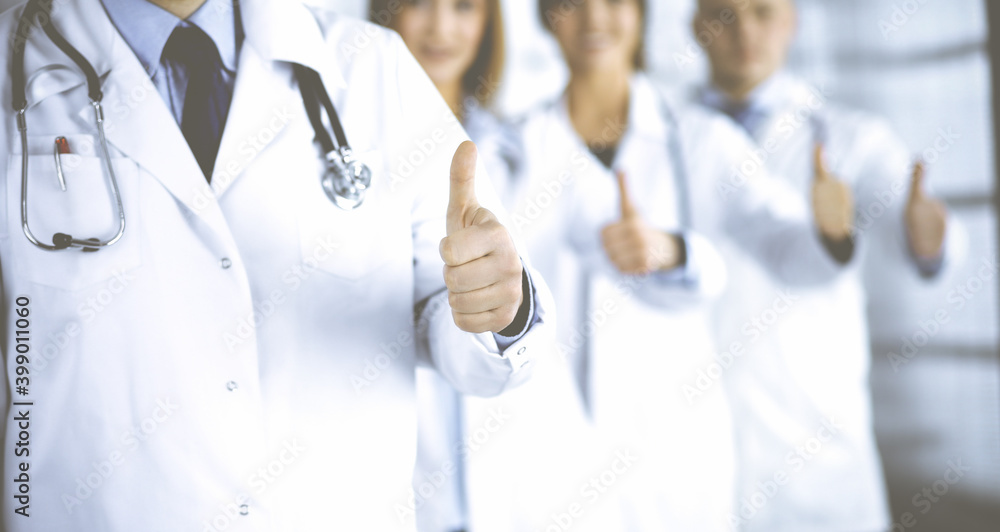Group of unknown doctors standing as a team with thumbs up in a hospital. Medical help, insurance in health care, best disease treatment and medicine concept Group of unknown doctors standing as a team with thumbs up in a hospital. Medical help, insurance in health care, best disease treatment and medicine concept