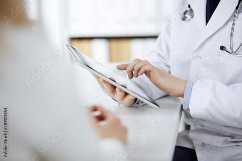Unknown male doctor and patient woman discussing current health examination while sitting in clinic and using tablet computer. Perfect medical service in hospital. Medicine and healthcare concept