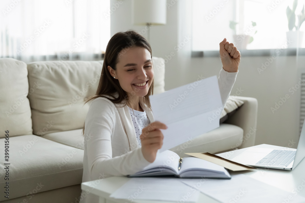Excited young woman reading good news in paper letter, showing yes gesture, sitting at work table in living room, celebrating job promotion or great exam results, money refund, getting scholarship Excited young woman reading good news in paper letter, showing yes gesture, sitting at work table in living room, celebrating job promotion or great exam results, money refund, getting scholarship