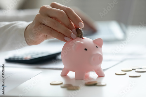Close up young woman putting coin into pink piggy bank, saving money, female calculating bills, using calculator, checking domestic financial documents, planning budget, investment strategy