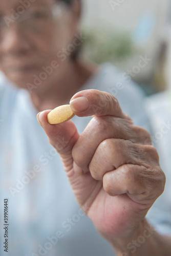 Close up view of aged senior asian female's hand holding a vitamin tablet with fingers, supplements for elderly people, health care of senior citizens concept.
Selective focus. photo