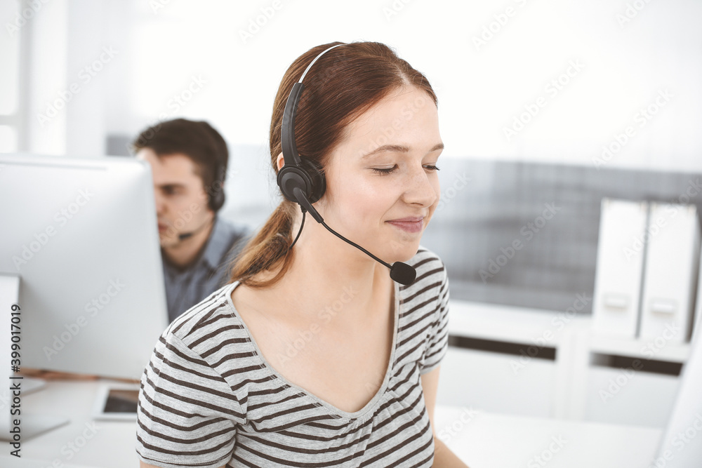Casual dressed young woman using headset and computer while talking with customers online. Group of operators at work. Call center, business concept Casual dressed young woman using headset and computer while talking with customers online. Group of operators at work. Call center, business concept