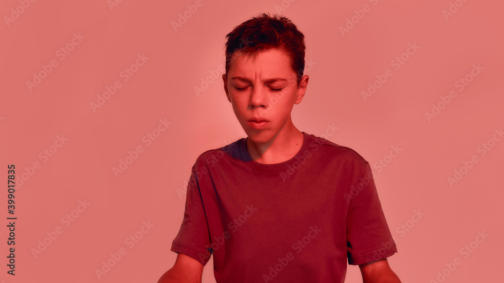 Portrait of teenaged disabled boy with cerebral palsy keeping his eyes closed, suffering from pain, posing isolated over red light background Portrait of teenaged disabled boy with cerebral palsy keeping his eyes closed, suffering from pain, posing isolated over red light background