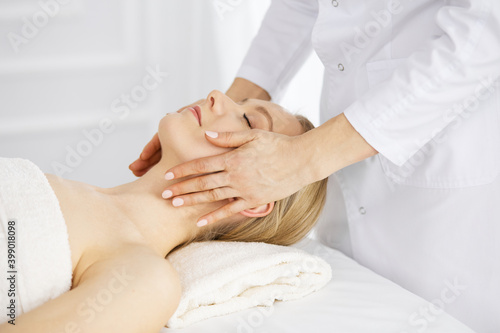 Schilderij op canvas Beautiful caucasian woman enjoying facial massage with closed eyes in spa salon