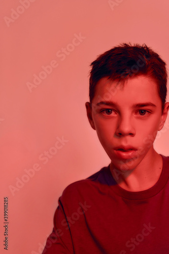 Close up portrait of teenaged disabled boy with cerebral palsy looking away, posing isolated over red light background