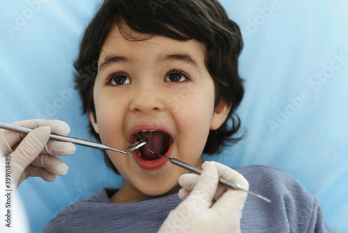 Cute arab boy sitting at dental chair with open mouth during oral checking up with doctor. Visiting dentist office. Stomatology concept