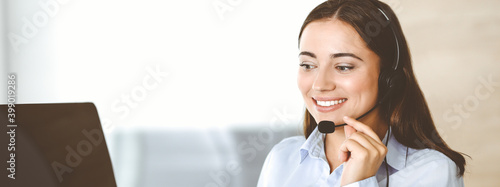 Brunette female customer service representative in a headset is consulting clients online. Call center and business people concept