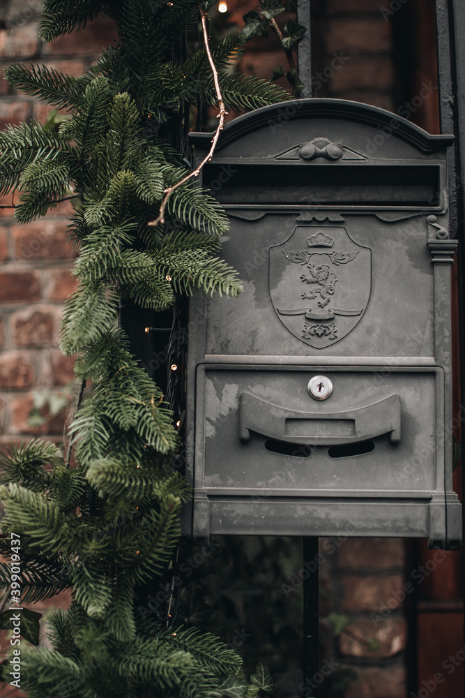 Old black vintage mailbox decorated with sprigs of fir for Christmas holidays. Old bricks house.