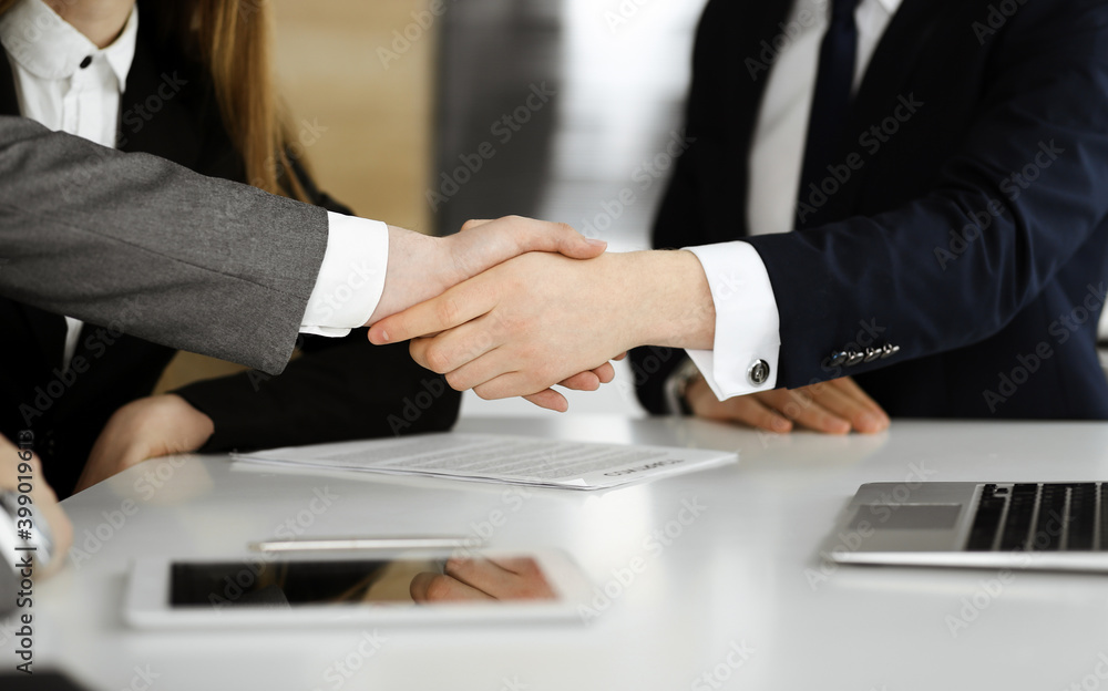 Unknown businessman shaking hands with his colleague or partner above the glass desk in modern office, close-up. Business people group at meeting Unknown businessman shaking hands with his colleague or partner above the glass desk in modern office, close-up. Business people group at meeting