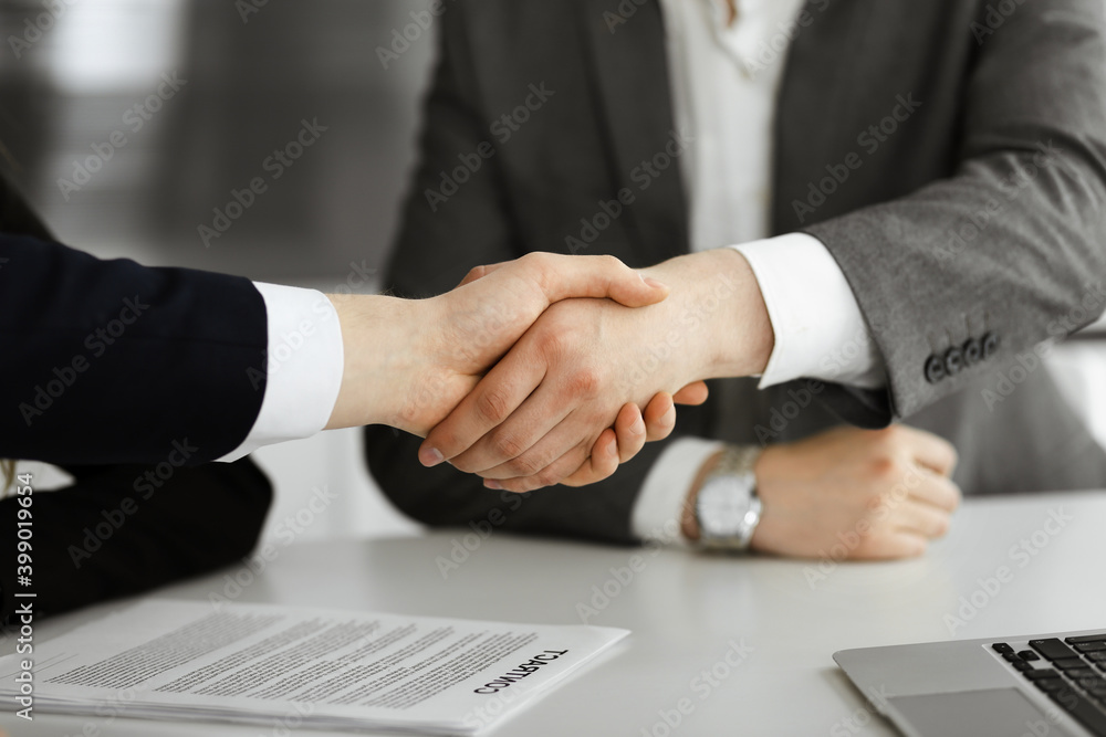 Unknown businessman shaking hands with his colleague or partner above the glass desk in modern office, close-up. Business people group at meeting Unknown businessman shaking hands with his colleague or partner above the glass desk in modern office, close-up. Business people group at meeting
