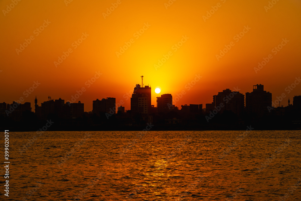 Orange sunset on the Nile river, the sun hides in the buildings of the city of Cairo in the background. Africa