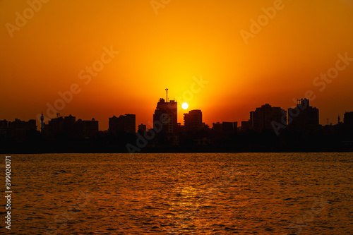 Orange sunset on the Nile river, the sun hides in the buildings of the city of Cairo in the background. Africa © unai