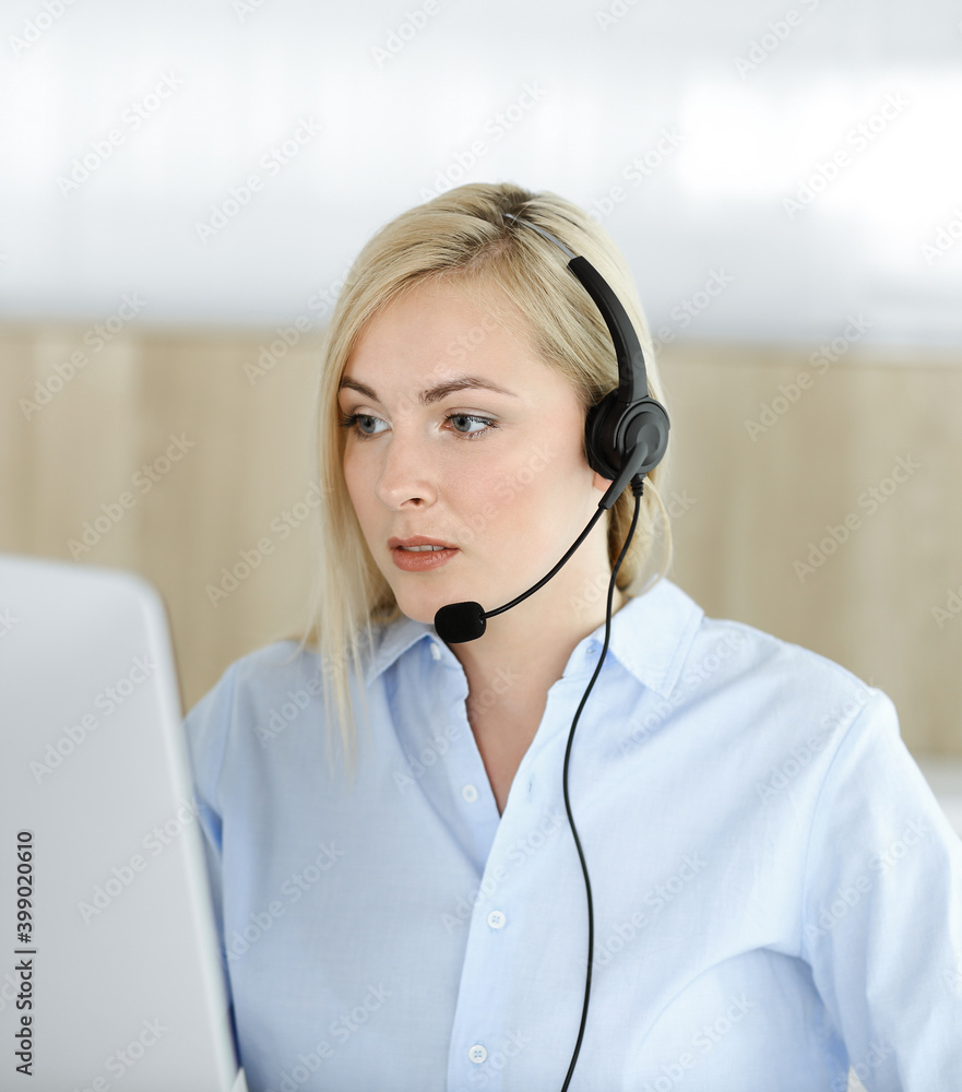 Blonde business woman sitting and communicated by headset in call center office. Concept of telesales business or home office occupation Blonde business woman sitting and communicated by headset in call center office. Concept of telesales business or home office occupation