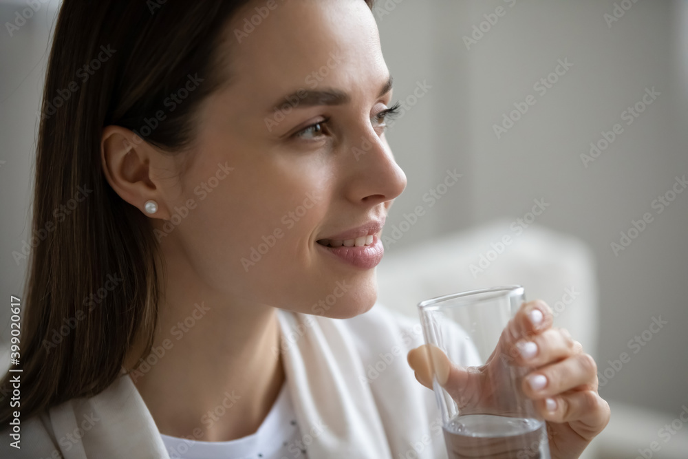 Close up side view smiling beautiful young woman with smooth skin holding glass of fresh mineral water, healthy lifestyle and good daily habit concept, natural beauty, skincare and weight loss Close up side view smiling beautiful young woman with smooth skin holding glass of fresh mineral water, healthy lifestyle and good daily habit concept, natural beauty, skincare and weight loss