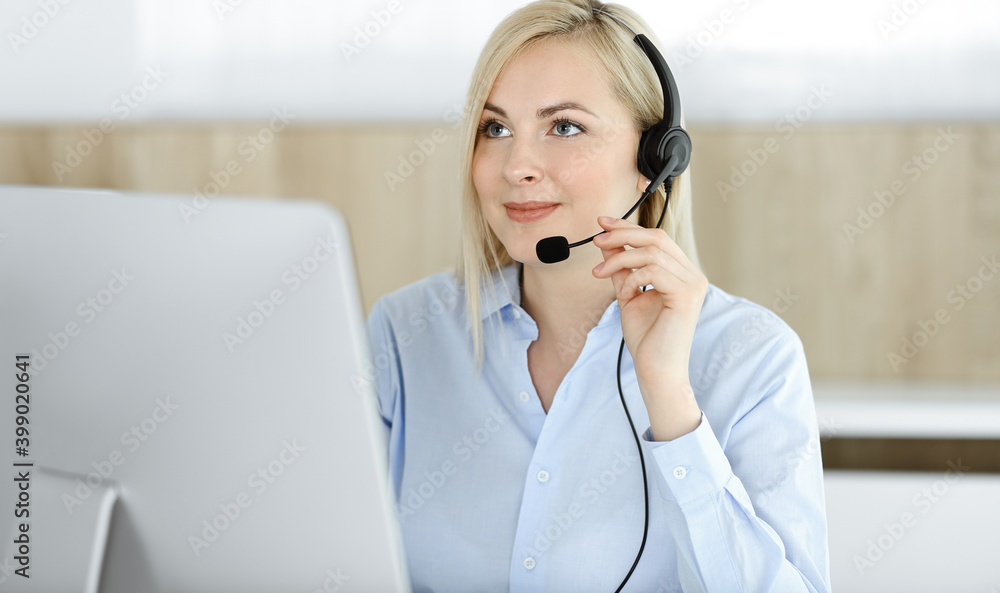 Blonde business woman sitting and communicated by headset in call center office. Concept of telesales business or home office occupation Blonde business woman sitting and communicated by headset in call center office. Concept of telesales business or home office occupation