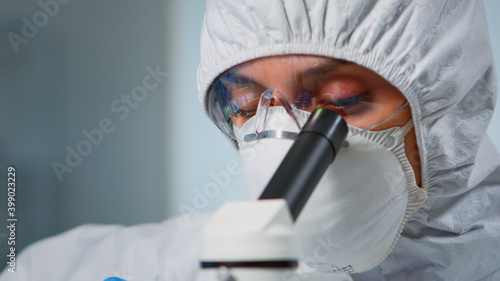 Close up of experienced biologist in ppe suit working on microscopes in equipped laboratory. Chemist in coverall examining vaccine evolution using high tech researching diagnosis against covid19 virus