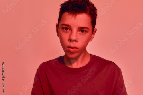 Close up portrait of teenaged disabled boy with cerebral palsy looking at camera, posing isolated over red light background
