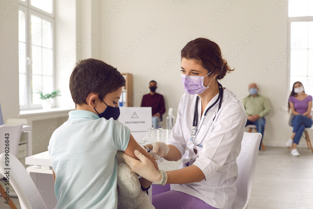 Brave little boy in a face mask looking at the needle while getting a flu vaccine Brave little boy in a face mask looking at the needle while getting a flu vaccine