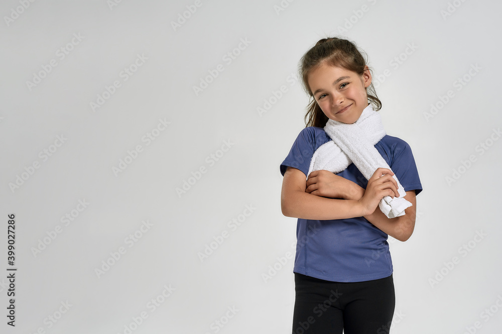 Little sportive girl child in sportswear smiling at camera, holding towel around her neck while standing isolated over white background Little sportive girl child in sportswear smiling at camera, holding towel around her neck while standing isolated over white background