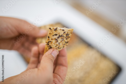 Female hand holding multi-seed crispbread above a tray with seeds and nuts