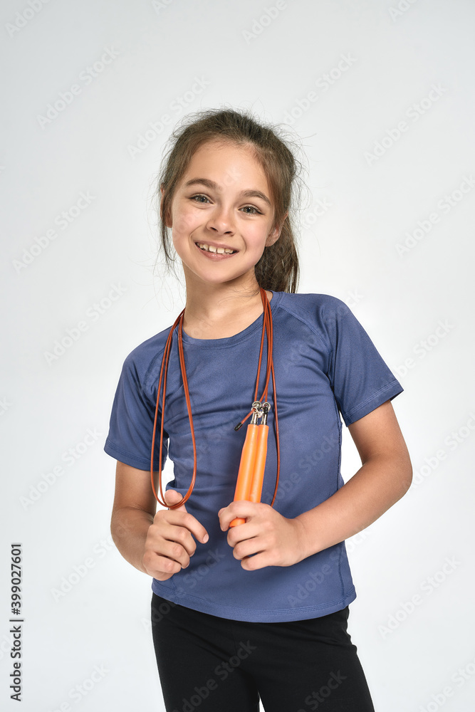 Little sportive girl child in sportswear smiling at camera, standing with jump rope while posing isolated over white background Little sportive girl child in sportswear smiling at camera, standing with jump rope while posing isolated over white background