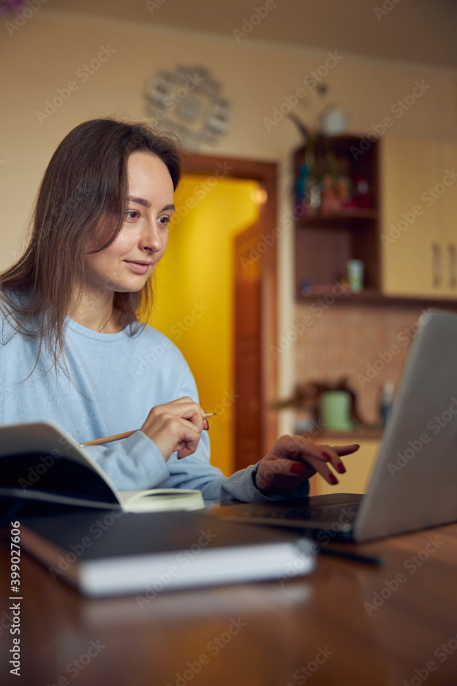 Young cheerful confident and happy freelancer woman is working on laptop at her kitchen at home