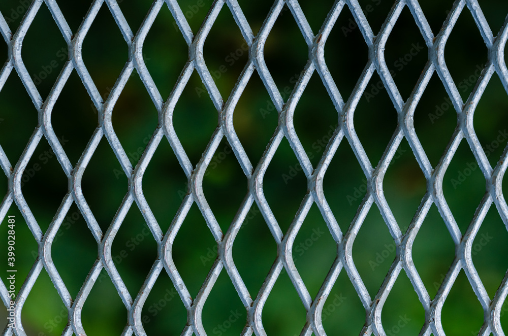 Fototapeta premium Silver grid of metal fence with blurred green color background.