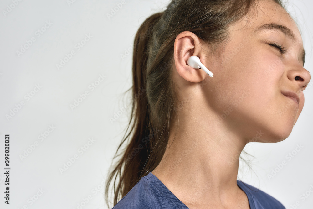 Close up portrait of little sportive girl child wearing earphones, listening to music, standing with eyes closed while posing isolated over white background Close up portrait of little sportive girl child wearing earphones, listening to music, standing with eyes closed while posing isolated over white background