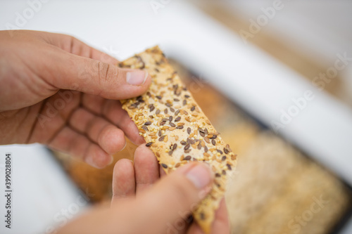 Female hand holding multi-seed crispbread above a tray with seeds and nuts