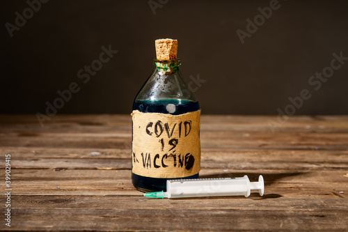Dirty artisanal bottle with a fake coronavirus vaccine made in unsanitary conditions and a syringe photo