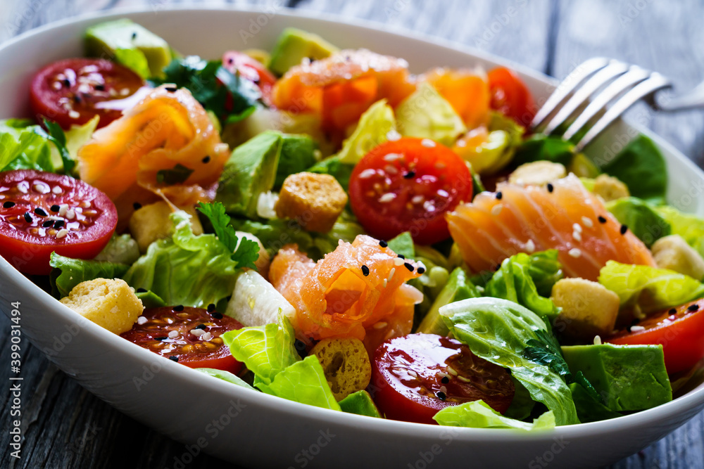 Salmon salad - smoked salmon with avocado and mix of vegetables on wooden table Salmon salad - smoked salmon with avocado and mix of vegetables on wooden table