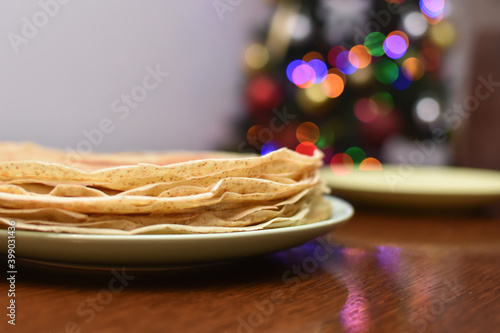 Stack of pancakes on table in front of Christmas tree. Pancakes with a Christmas light behind